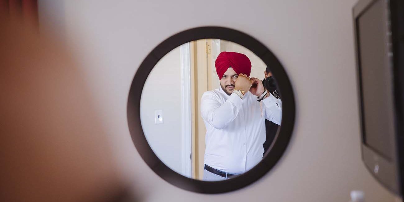 Groom adjusting his cufflinks while preparing for his wedding day, reflected in a mirror in Floral Park, New York