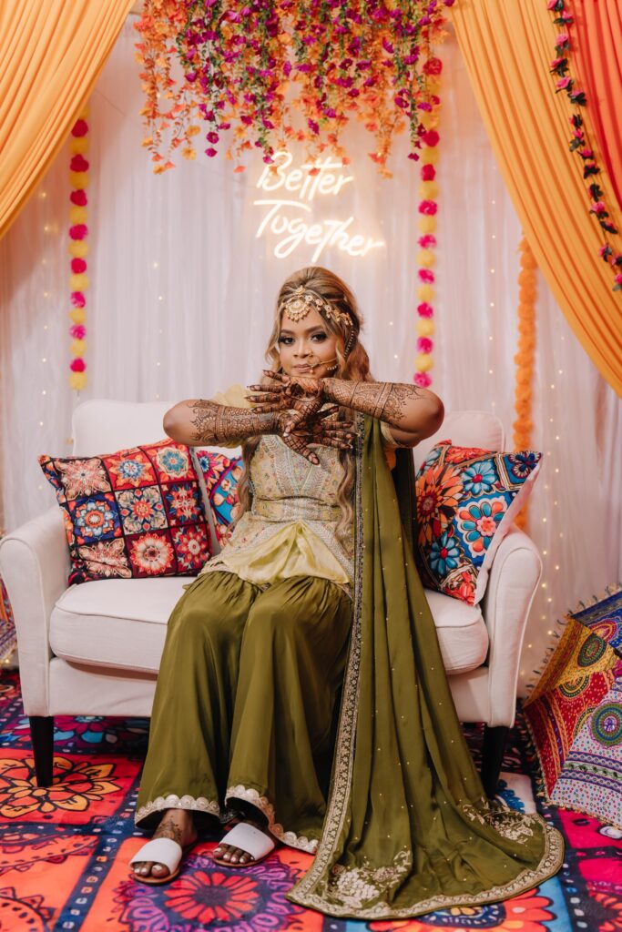Indian bride posing with detailed mehndi hands during a colorful mehndi ceremony setup with floral decor in Floral Park, New York