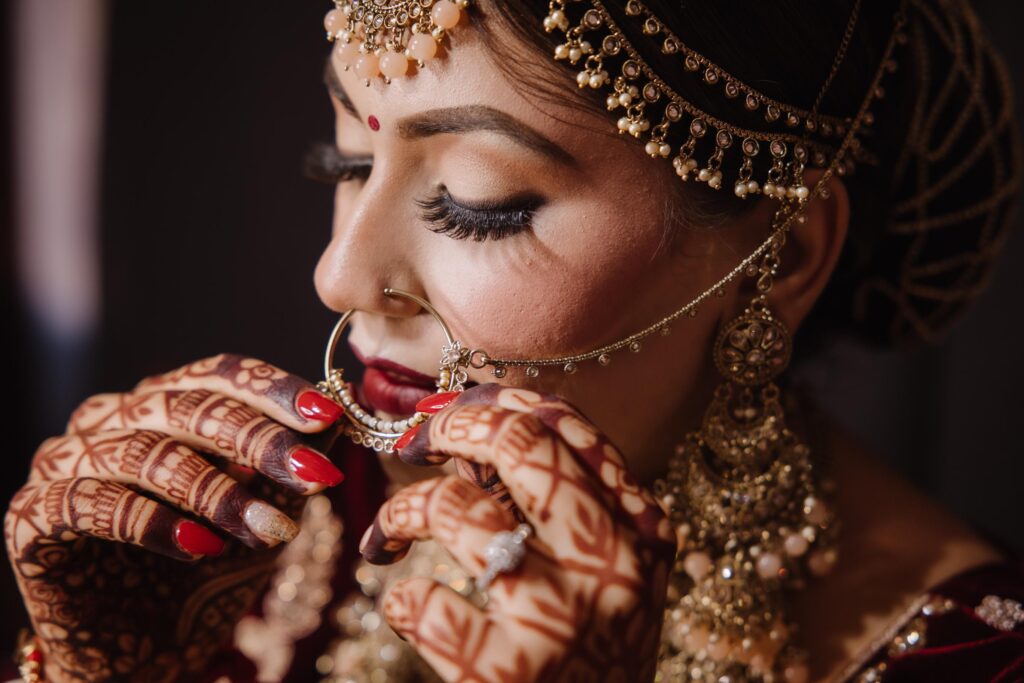 Close-up of Indian bride adjusting her nath (nose ring), showing mehndi, red nails and traditional gold jewelry — Citi Events Productions.